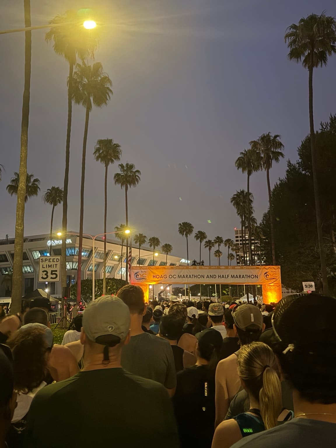 Runners waiting beneath palm trees at the OC Marathon start line before dawn.